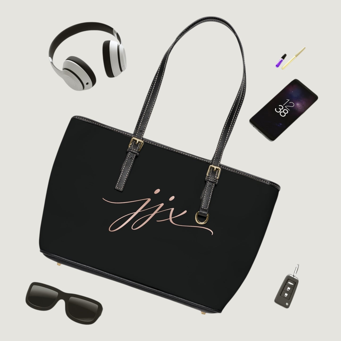 JJ Luxury House zwarte PU lederen schoudertas met goudkleurige gespen en JJX logo, omringd door dagelijkse accessoires.